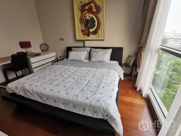 公寓 出租在Watthana, Bangkok - 主卧配大床、书桌与墙面艺术画，转角落地窗可望绿景。