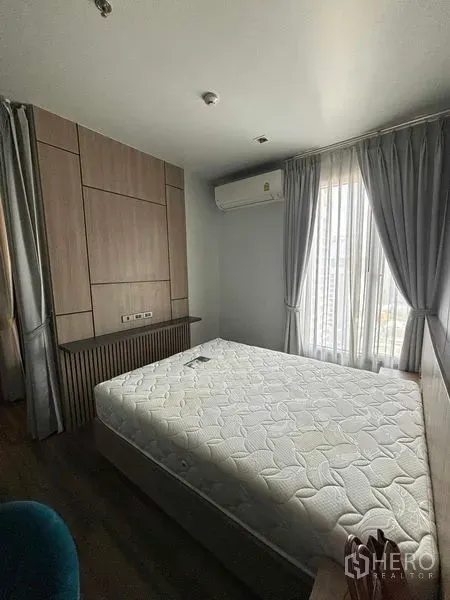 Condominium for rent or sale in Watthana, Bangkok - Bright bedroom with queen bed, built-in headboard, air conditioner and sheer curtains.
