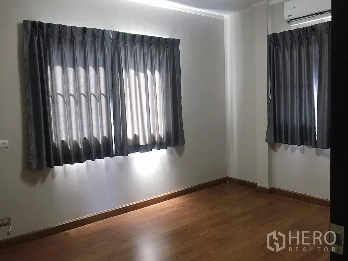 Detached House for sale in Lat Krabang, Bangkok - Cozy bedroom with wood flooring, air conditioner and twin windows with blackout curtains.