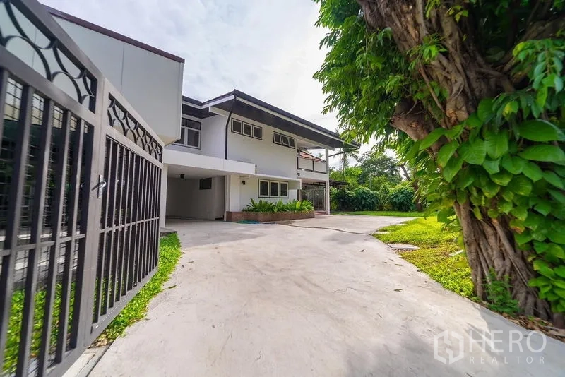 带办公室的家 出租在Khlong Toei, Bangkok - 带大门的车道通向两层家庭办公楼，旁有大树与草坪。
