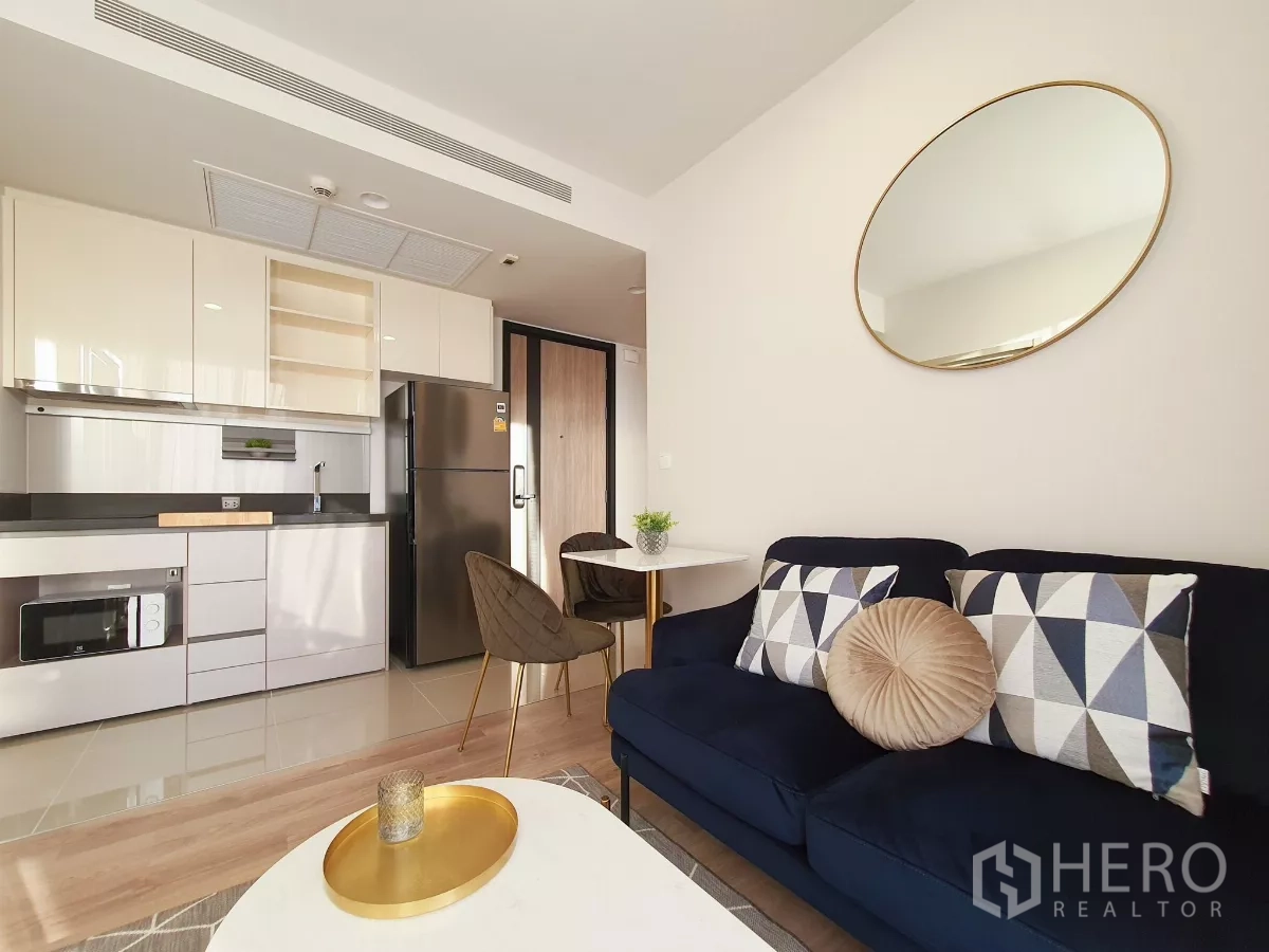 Condominium for rent in Khlong Toei, Bangkok - Open‑plan kitchen with glossy cabinets, fridge and cozy sofa corner.
