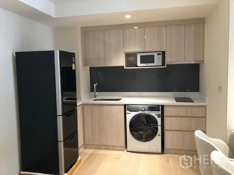 Condominium for rent in Watthana, Bangkok - Fitted kitchen with light wood cabinets, fridge, microwave, cooktop and washer-dryer.
