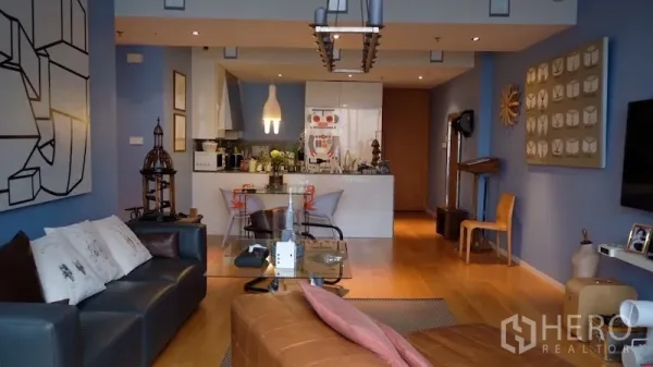 Condominium for rent or sale in Sathon, Bangkok - Open‑plan living room with blue accent walls, wood floors and a chandelier facing the kitchen.