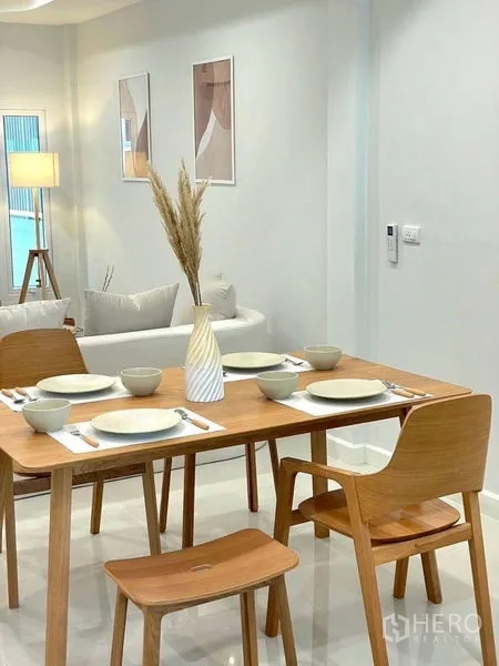 Townhouse for sale in Khlong Toei, Bangkok - Wood dining table set for four with plates and bowls beside the living area.