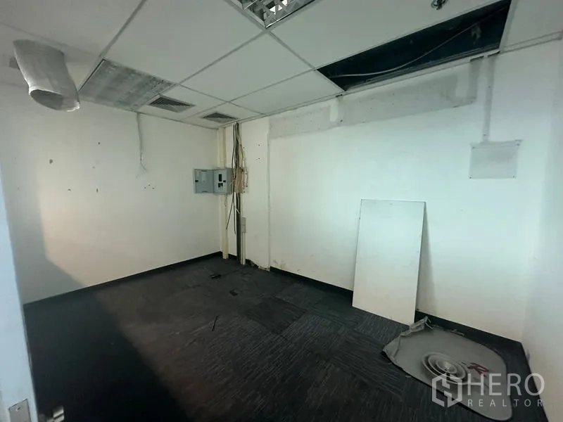 Office Space for rent in Watthana, Bangkok - Vacant utility room with exposed ceiling tiles, electrical panel, and dark carpet in Bangkok office.