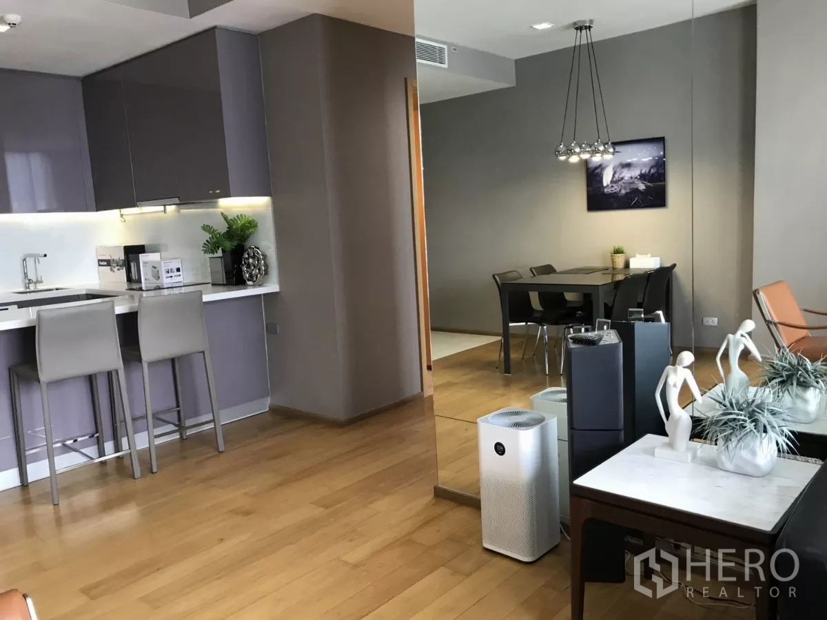 Condominium for rent in Watthana, Bangkok - Open kitchen and dining zone with a mirror feature wall and two bar stools.