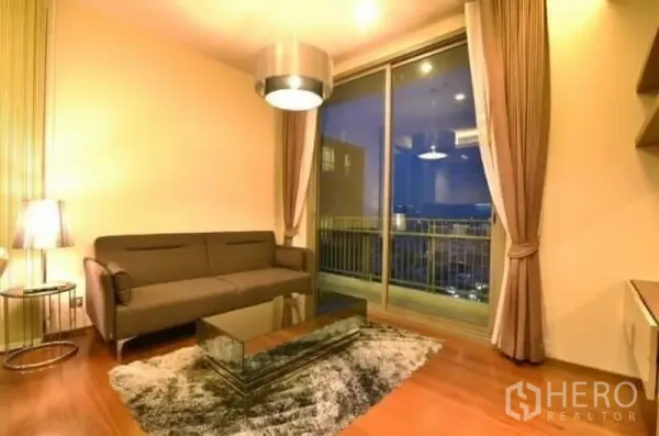 คอนโด ให้เช่าในWatthana, Bangkok - ห้องนั่งเล่นบรรยากาศอบอุ่น โซฟา โต๊ะกลางกระจก พรม และประตูกระจกบานเลื่อนออกสู่ระเบียงวิวเมืองยามค่ำคืน