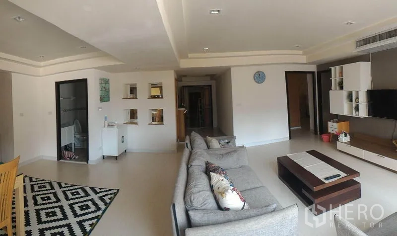 Condominium for rent or sale in Watthana, Bangkok - Open‑plan living and dining space with sofa set, patterned rug and bright tray ceiling.