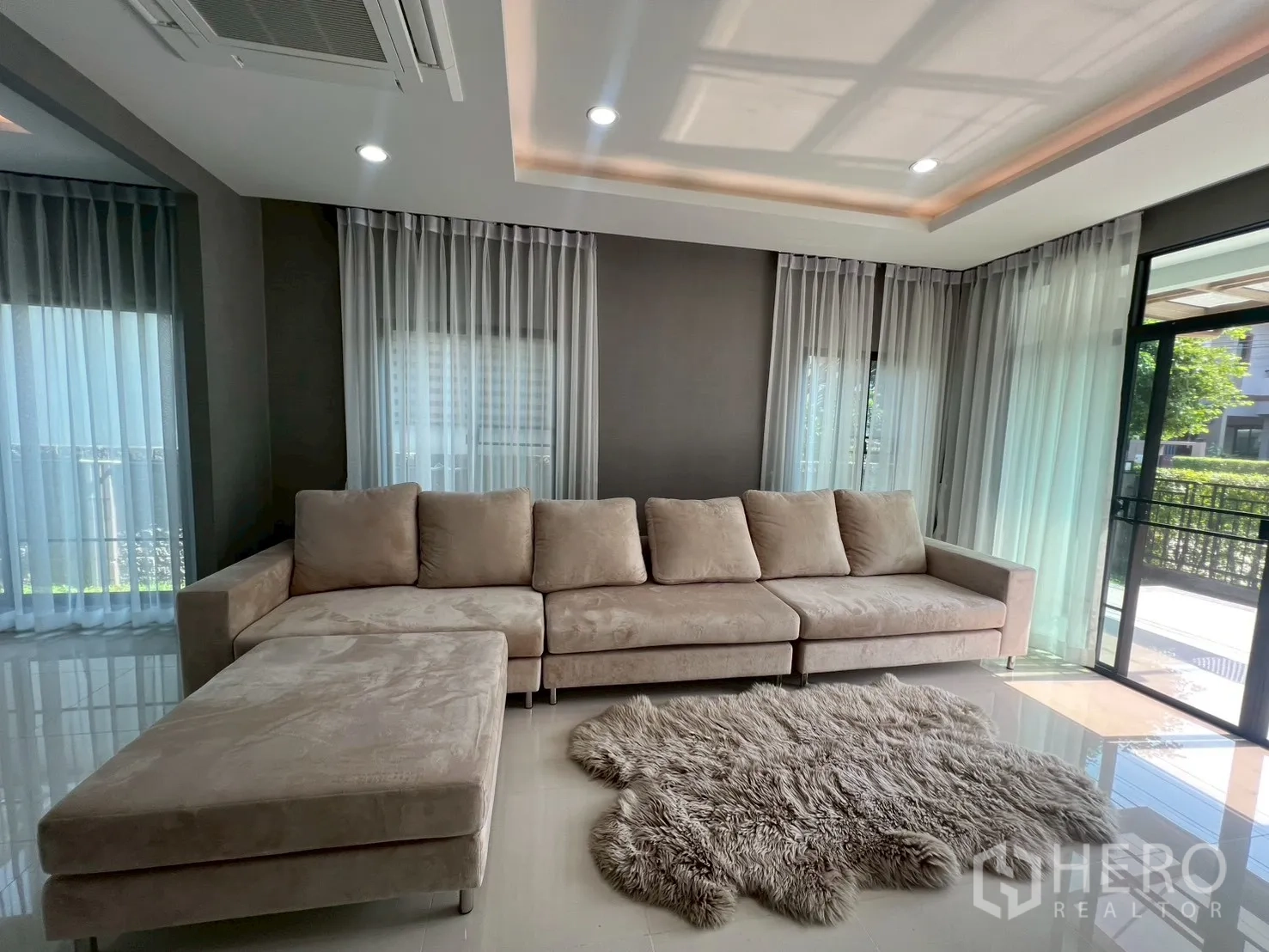 独立式住宅 出租或出售在Bang Phli, Samut Prakan - 一层客厅，米色L型沙发和落地窗。