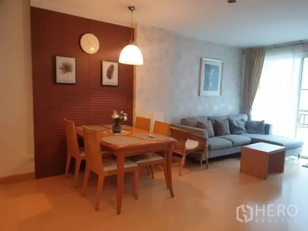 Condominium for rent in Watthana, Bangkok - Cozy dining area with wooden table and pendant light beside a bright living room and L-shaped sofa.