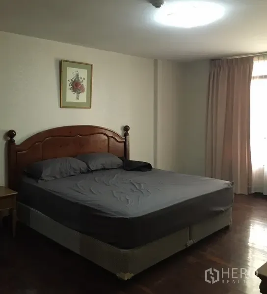 Condominium for rent in Watthana, Bangkok - Spacious master bedroom with a large bed, wooden headboard and curtained window letting in natural light.