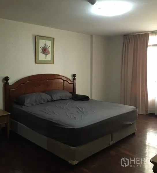 Condominium for rent in Watthana, Bangkok - Spacious master bedroom with a large bed, wooden headboard and curtained window letting in natural light.