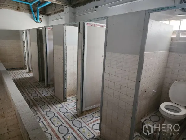 Factory for rent or sale in Khlong Toei, Bangkok - Multi-stall restroom with tiled partitions and patterned floor in an industrial building.