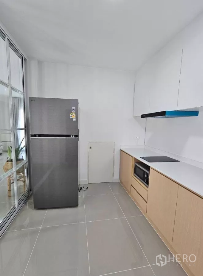 Detached House for rent in Bang Phli, Samut Prakan - Kitchen corner with stainless refrigerator, induction hob and white upper cabinets.