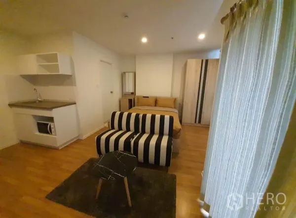 公寓 出售在Chatuchak, Bangkok - 开放式一居室，带小厨房、床、条纹沙发与落地窗帘。