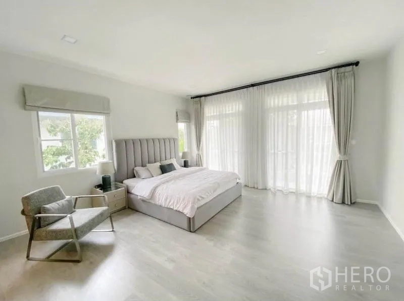 独立式住宅 出租在Prawet, Bangkok - 宽敞主卧，King尺寸床与躺椅，整面窗帘通向阳台。