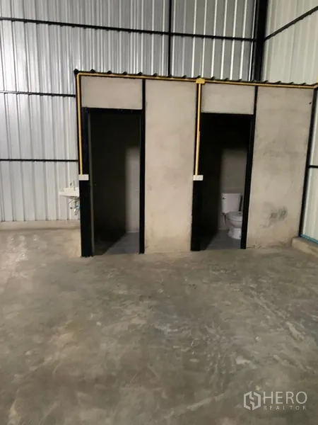 Warehouse for rent in Khan Na Yao, Bangkok - On-site facilities showing two concrete restroom stalls with a sink inside the warehouse.