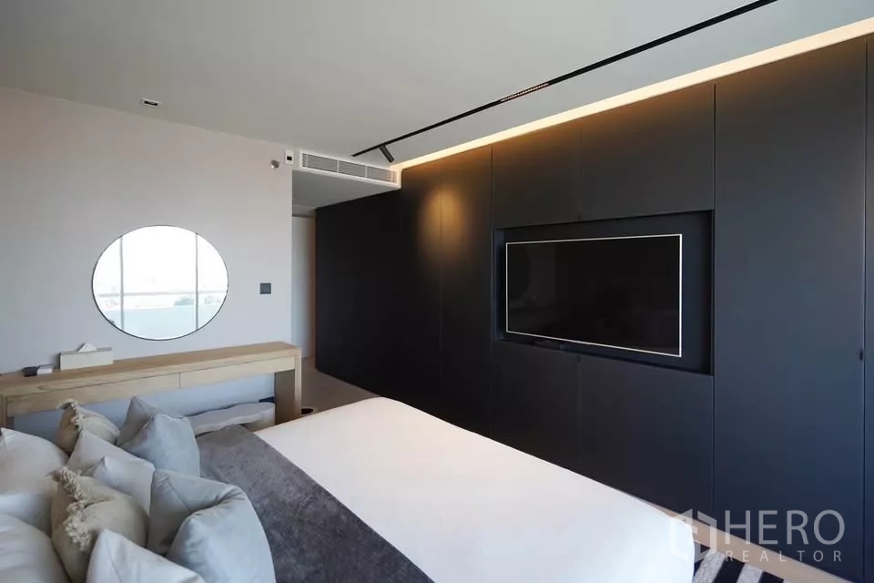 公寓 出租在Bang Phlat, Bangkok - 极简卧室，深色一体电视墙与浅色梳妆台相映成趣。