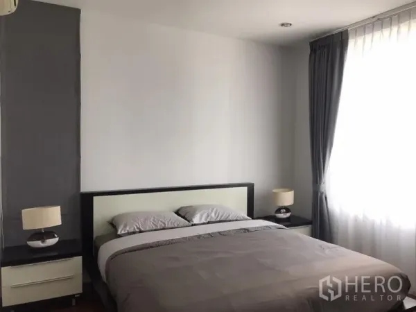 Condominium for rent in Khlong Toei, Bangkok - Cozy bedroom with queen bed, matching nightstands, lamps and a large window with sheer curtains.