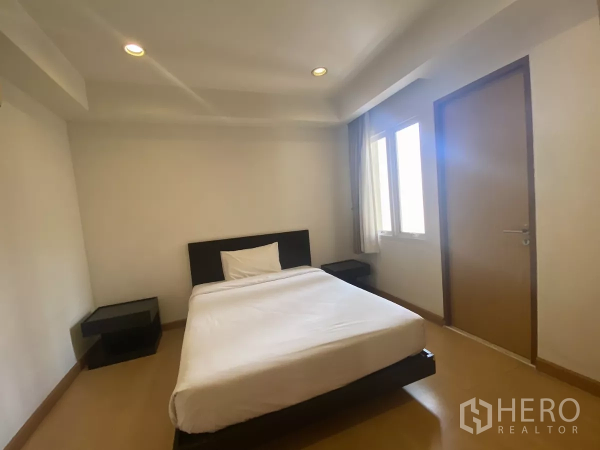 Condominium for rent in Watthana, Bangkok - Second bedroom with bed, twin side tables and natural light from corner windows.