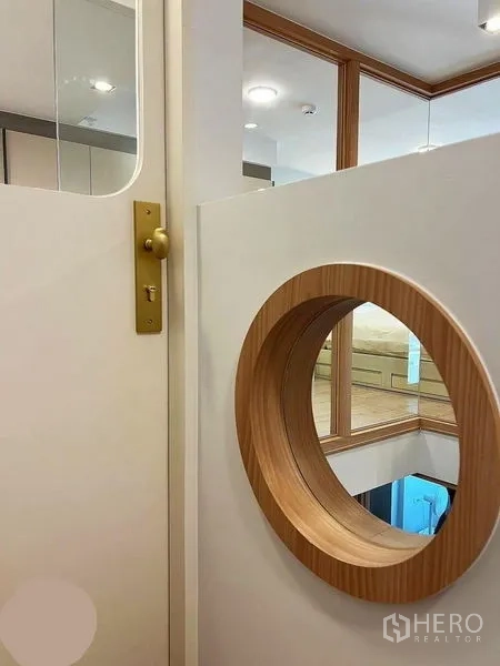 Condominium for rent in Huai Khwang, Bangkok - Close-up of a white door with brass handle and round wood-trimmed porthole window.