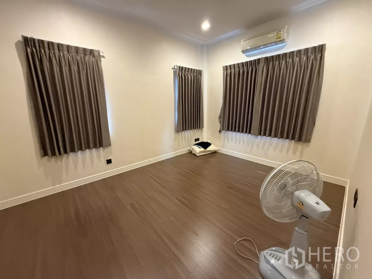 Detached House for rent in Bang Kapi, Bangkok - Spacious bedroom with wood floors, multiple curtained windows, and neutral walls.