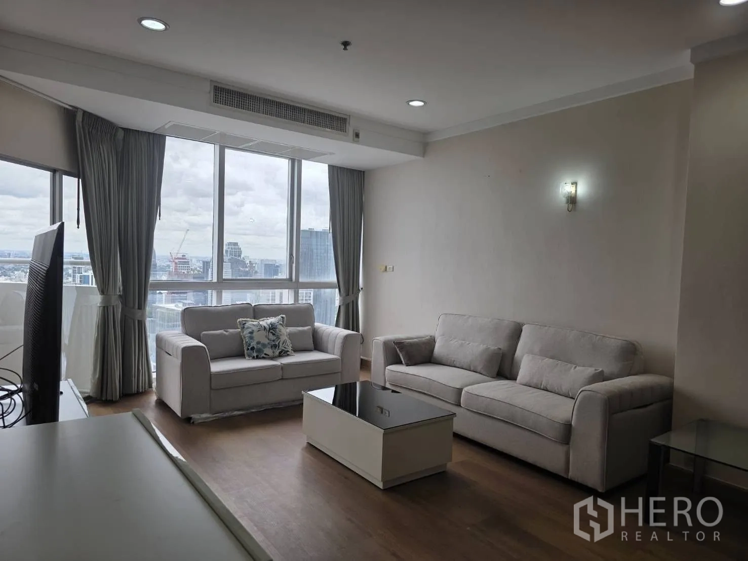 Condominium for rent in Khlong Toei, Bangkok - Bright living room with two grey sofas, coffee table and floor-to-ceiling windows overlooking Bangkok skyline.