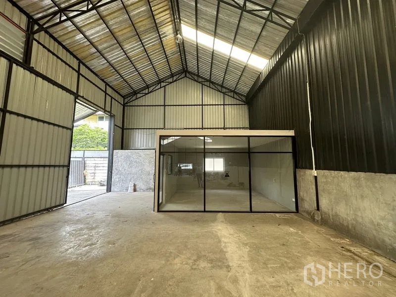 Warehouse for rent in Lat Phrao, Bangkok - Interior view toward the glass-walled office showing the steel-truss roof structure.