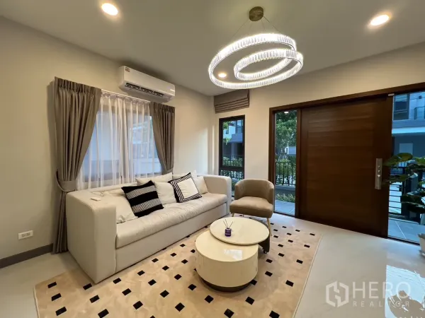 Detached House for rent in Bang Phli, Samut Prakan - Bright living room with large sofa, circular chandelier and wooden entrance door.