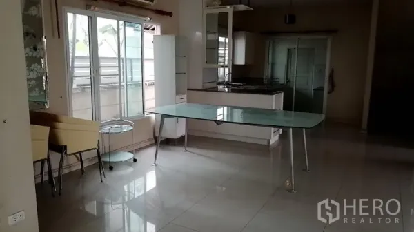 Detached House for rent in Lat Krabang, Bangkok - Dining area with a glass-top table beside bright windows and a compact kitchen.