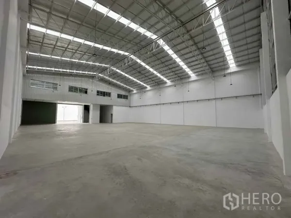 Factory for rent in Khlong Luang, Pathum Thani - Large factory floor featuring translucent roof strips and upper-level office windows overlooking the floor.