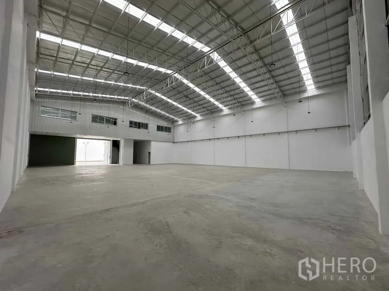 Factory for rent in Khlong Luang, Pathum Thani - Large factory floor featuring translucent roof strips and upper-level office windows overlooking the floor.