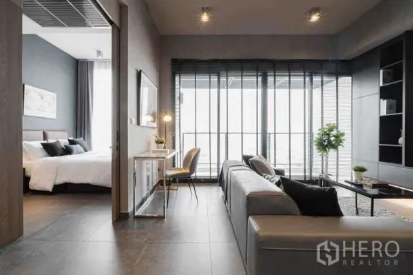 Condominium for rent in Watthana, Bangkok - Loft-style lounge with work desk, sofa and full-height windows beside the bedroom.