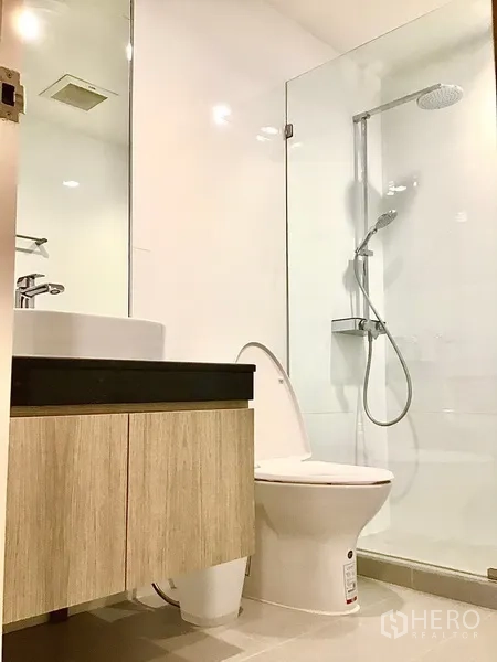 Condominium for rent in Pathum Wan, Bangkok - Clean bathroom with glass-enclosed shower, vanity and toilet.