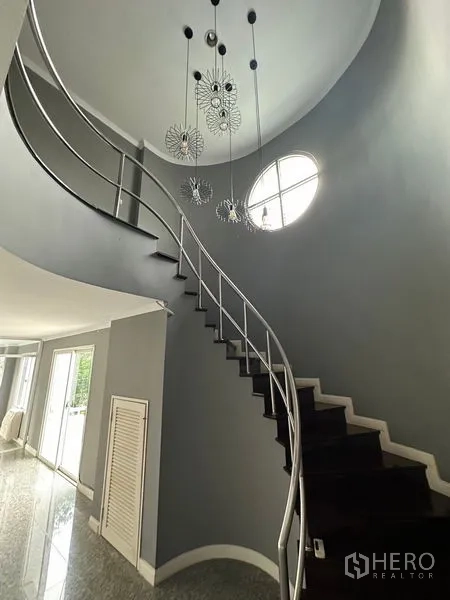 Townhouse for rent in Bang Kapi, Bangkok - Curved staircase with stainless rails, modern pendant lights and a round window.