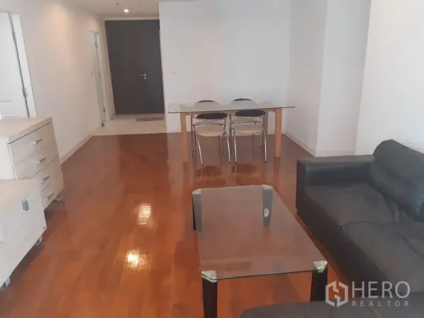 Condominium for rent in Khlong Toei, Bangkok - Open-plan living and dining area with wooden flooring, glass dining table for four and neutral walls.