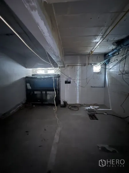Retail Space for rent in Watthana, Bangkok - Back utility room with exposed wiring, small windows and concrete floor in the retail unit.