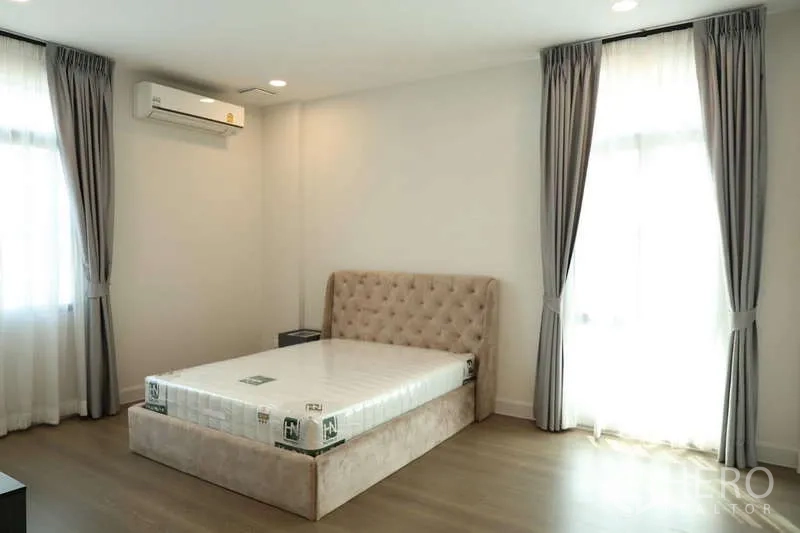 Detached House for rent or sale in Saphan Sung, Bangkok - Sunlit bedroom with upholstered bed, wood floor and double curtains.