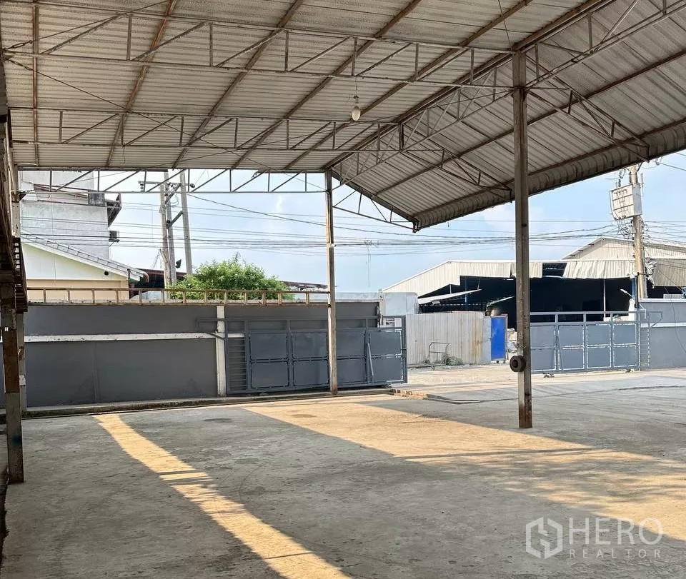 Factory for rent in Samut Prakan - Covered loading area with steel roof looking toward the gated entrance.