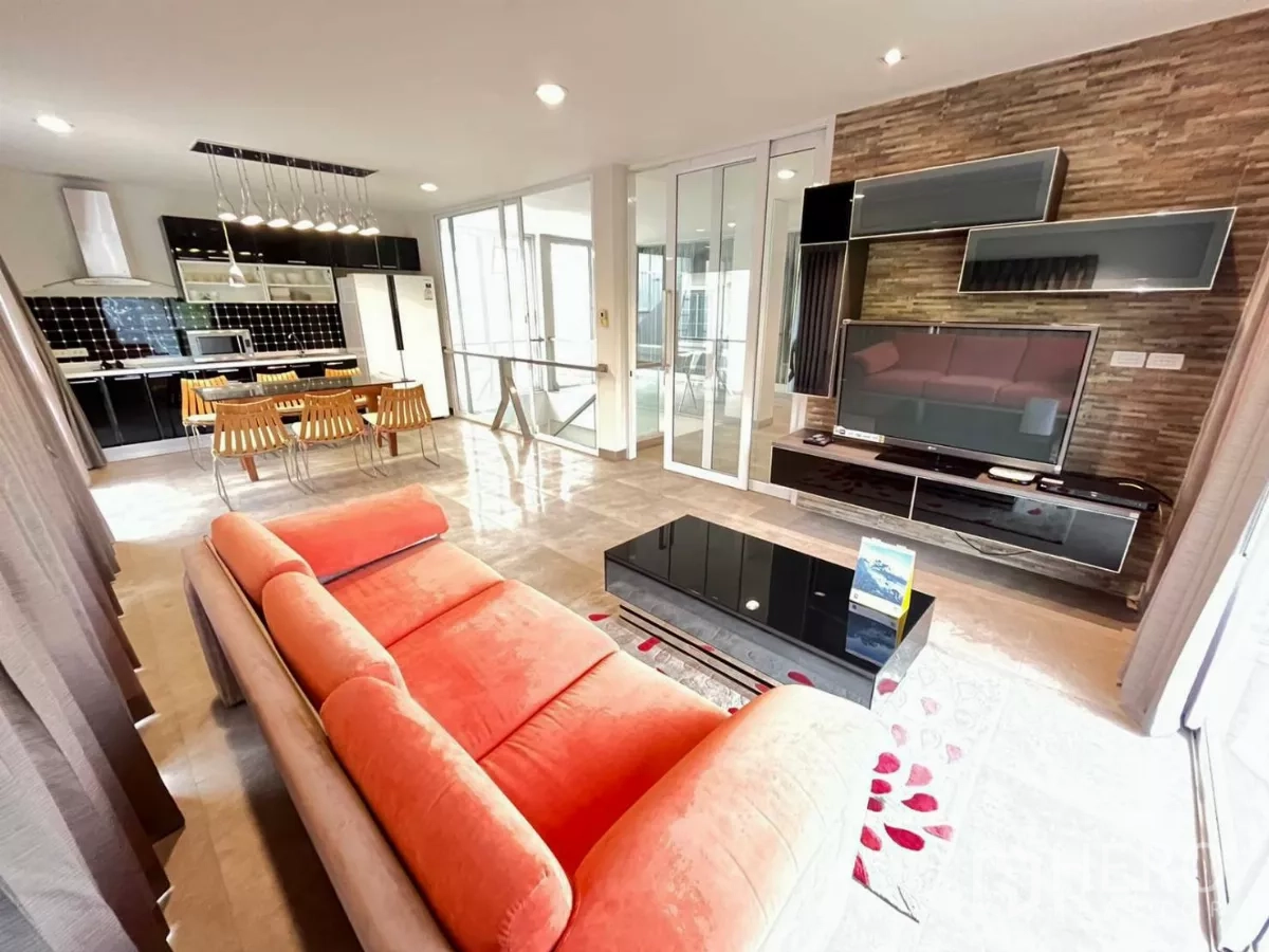 Home Office for rent in Khlong Toei, Bangkok - Living area with orange sofa, TV wall unit and adjoining kitchen with dining table.