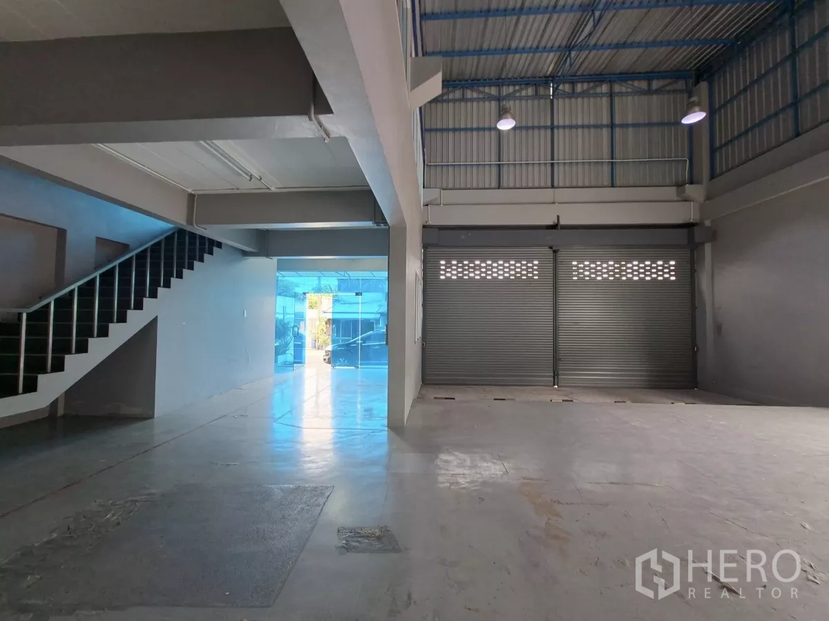 Warehouse for rent in Suan Luang, Bangkok - Open warehouse floor with 7‑meter high ceiling, steel beams and twin roller doors for loading.
