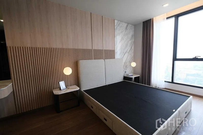 Condominium for rent in Khlong Toei, Bangkok - Master bedroom with textured wood paneling, upholstered headboard, and city-view window.
