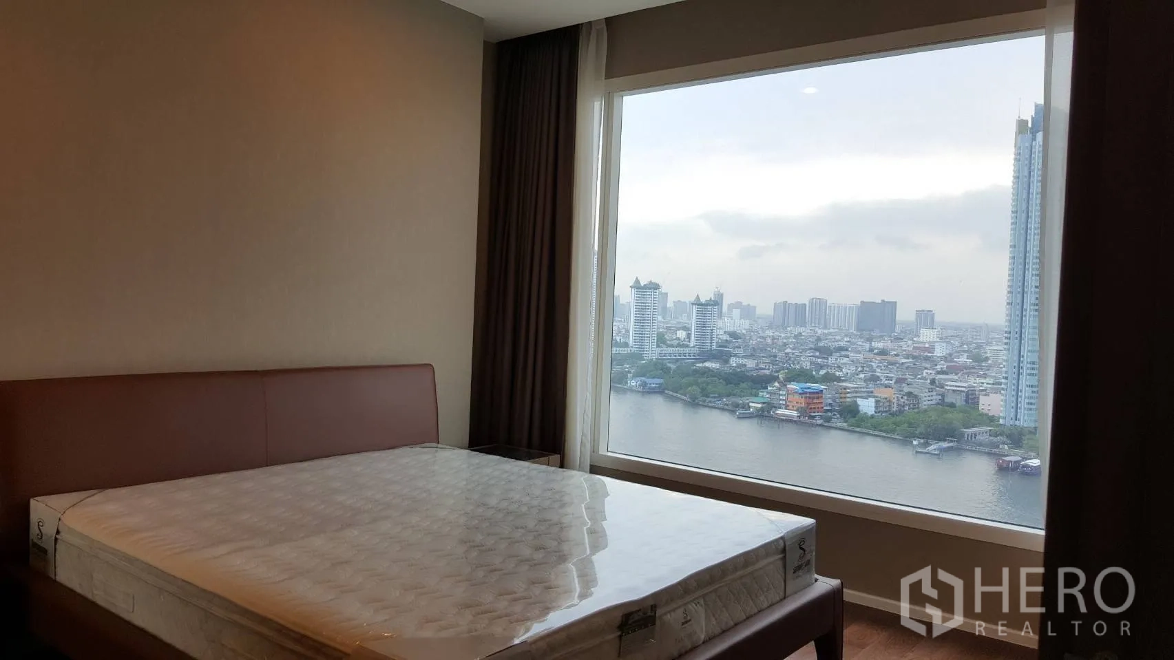 Condominium for rent in Bang Kho Laem, Bangkok - Bedroom with large picture window framing Chao Phraya River and city skyline views in a neutral-toned Bang Kho Laem condominium.