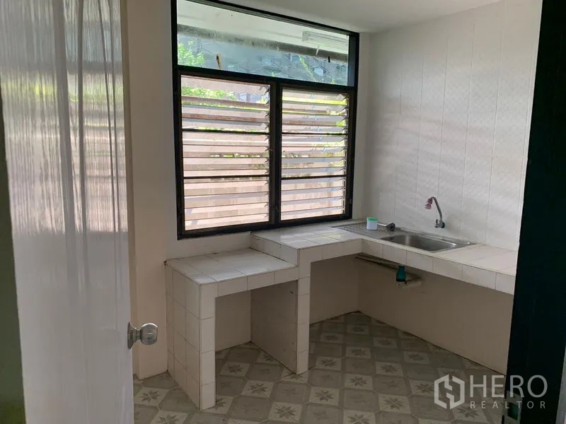 Detached House for rent in Khlong Toei, Bangkok - Simple Thai-style kitchen with tiled counters, single sink and louvered window.