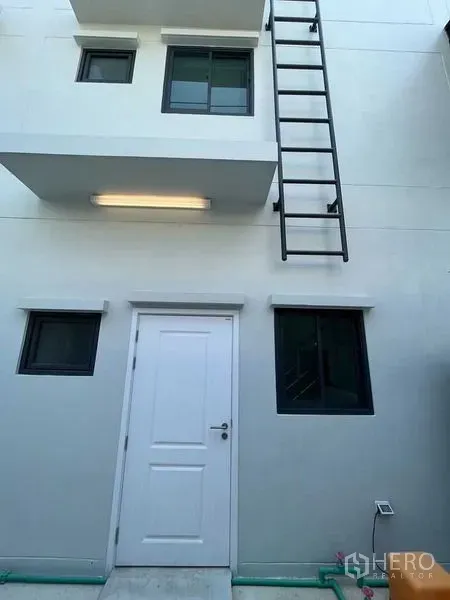 带办公室的家 出租 - 建筑后侧带白色服务门、窗户与外置金属梯。