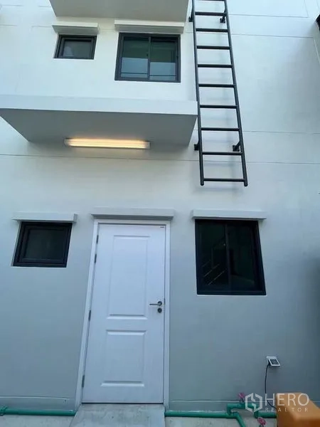 带办公室的家 出租 - 建筑后侧带白色服务门、窗户与外置金属梯。