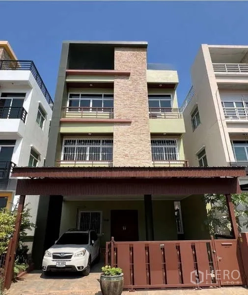 带办公室的家 出租或出售在Min Buri, Bangkok - 三层居家办公楼外立面，砖饰面、阳台与带顶车位及金属大门。