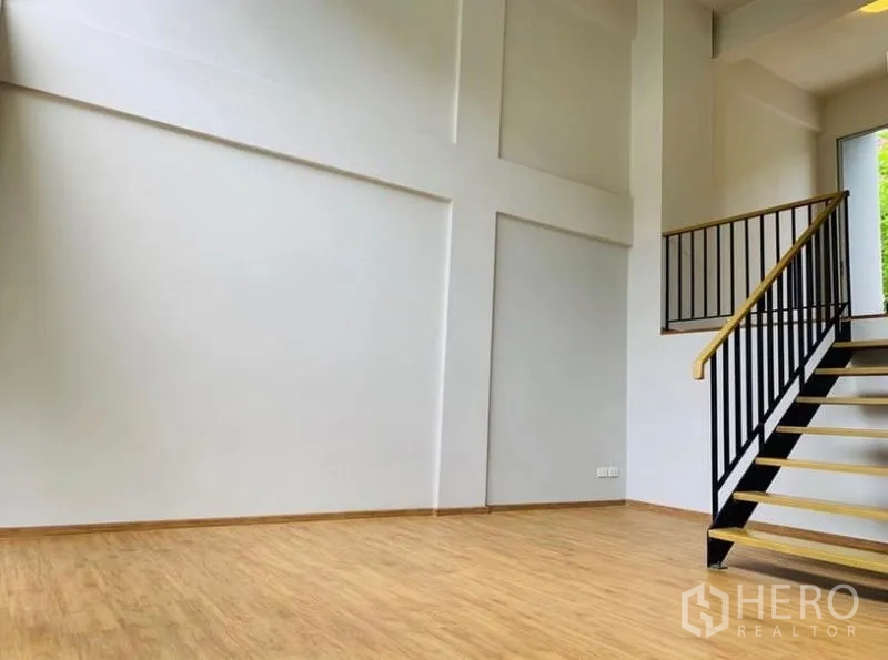 Home Office for rent - Spacious white-walled room with high ceiling and black metal stair railing on wood flooring.