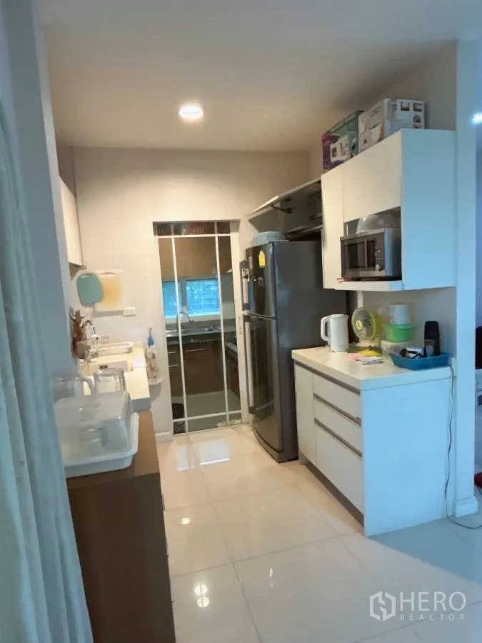 Detached House for sale in Bang Kapi, Bangkok - Pantry and secondary kitchen corridor with refrigerator and white cabinets.