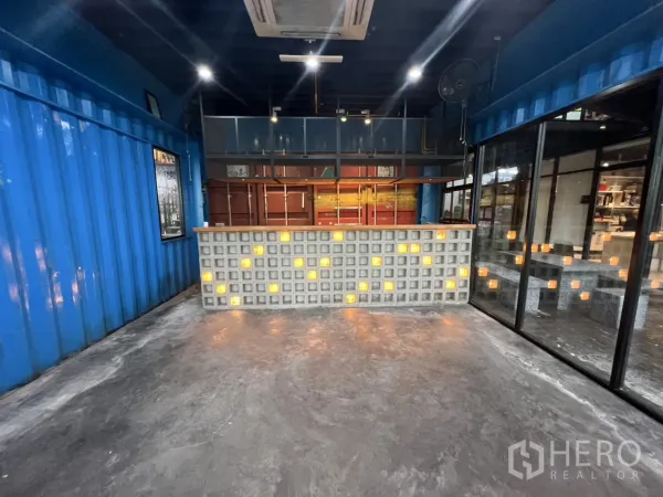 零售空间 出租 - 正面展示发光玻璃砖服务台，背景为金属搁架的集装箱风商铺。